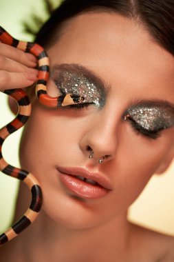 Büyüleyici genç bir kadın, çarpıcı bir yılanla etkileşime girer ve parlak makyajını gözler önüne serer..