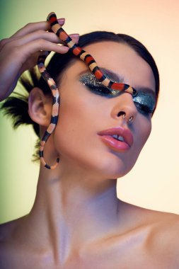 Genç bir kadın kendine güvenen bir yılanla poz veriyor, canlı renklerle güzelliğini vurguluyor..