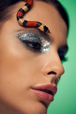 Genç bir kadın, alnına şakacı bir şekilde örtülmüş yılanla zarif poz verir, cazibe ve tehlikeyi birbirine karıştırır..