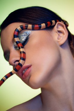 Genç bir kadın kendine güvenerek poz veriyor, büyüleyici bir şekilde üzerine bir yılan örterek..