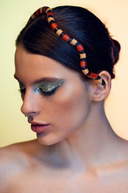 Göz kamaştırıcı makyajlı genç bir kadın zarif bir şekilde poz verirken bir yılan başının üstünde duruyor..