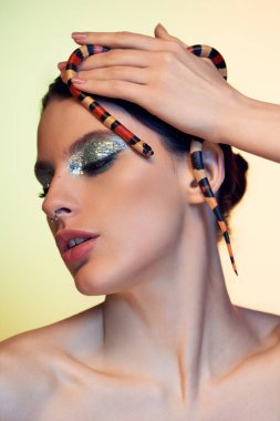 Çekici bir kadın zarif pozlar veriyor, güzelliğini ve saçında bir yılanı vurguluyor..