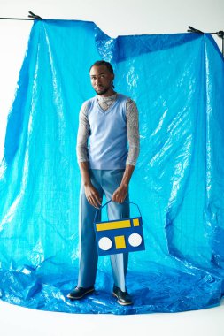 Şık bir genç adam dikkat çekici bir mavi arka plana karşı eşsiz bir kıyafet sergiliyor..