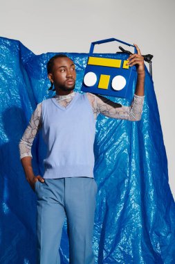 Kendinden emin genç bir adam canlı bir mavi arka plana karşı neşeli bir radyoyla poz veriyor..