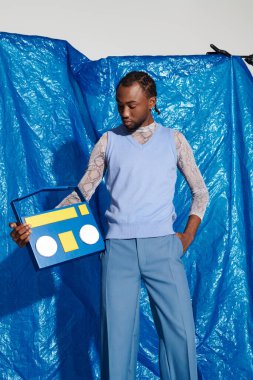 Yakışıklı bir genç, mavi bir arkaplan önünde güvenle dururken eşsiz bir aksesuar sergiliyor..