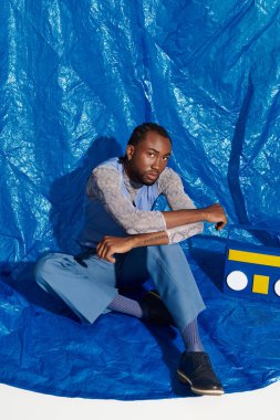 Şık, genç bir adam şık giyinmiş, cesur mavi bir zemin üzerinde oturuyor..