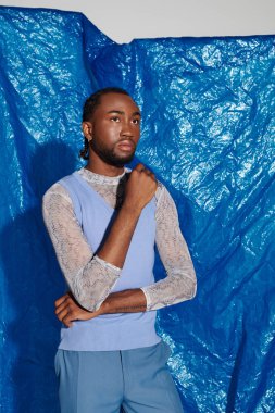 Genç bir adam dikkat çekici bir mavi arka plana karşı kendine güvenen bir şekilde poz verir..