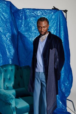 Çarpıcı bir mavi ortamda, genç adam moda ve duruş sergiliyor..