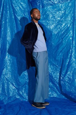 Şık bir genç adam kendine güvenerek poz verir, mavi bir ortamda zarafet saçar..