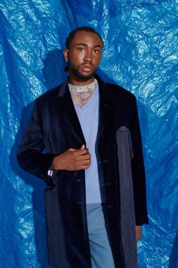 Şık bir genç adam canlı mavi bir tuvalin önünde zarif bir şekilde duruyor..