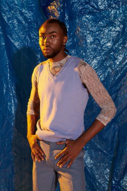 Çekici bakışları olan kendine güvenen genç bir adam sanatsal mavi bir arka plana karşı duruyor..