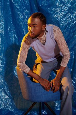 Şık bir genç adam canlı mavi bir zemine karşı düşünceli bir şekilde poz verir..