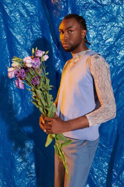 Afrika kökenli yakışıklı genç bir adam elinde bir buket çiçekle duruyor..