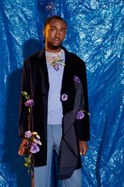 Zarif bir genç adam zarif çiçeklerle süslenmiş şık bir elbiseyle dimdik ayakta duruyor..