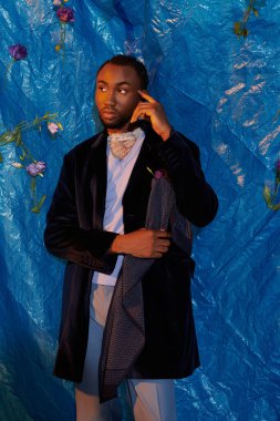 Şık giyinmiş kendine güvenen genç bir adam, çevresiyle mavi bir zemin üzerinde etkileşime girer..