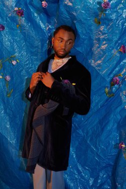 Şık bir genç adam kendine güveni tam, cesur mavi bir arka plana karşı duruyor, moda ve zarafet saçıyor..