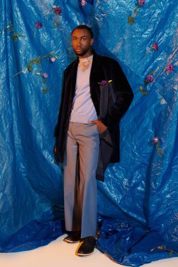 Şık bir genç adam kendine güvenerek mavi bir çiçek arkaplanının önünde duruyor..