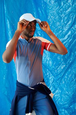 Kendine güvenen genç bir adam, mavi duvara çarpan bir göze karşı sportif bakışını sergiliyor..