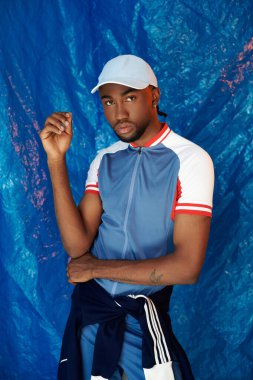 Kendinden emin genç bir adam canlı mavi bir arka plana karşı poz veriyor, somut stil ve karizma..