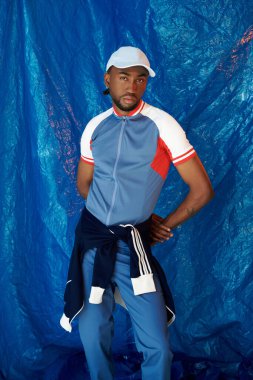 Şık bir genç adam gururla gururla ayakta duruyor parlak mavi bir arka plana karşı atletik giyim.