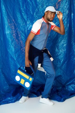 Şık bir genç, parlak mavi bir ortama karşı güvenli bir teyple poz veriyor..