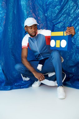 Genç adam çarpıcı bir mavi arkaplan karşısında renkli bir sanat eseriyle yaratıcı bir şekilde poz veriyor..