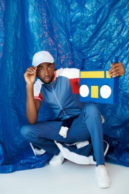 Yakışıklı genç adam kendine güveni tam bir şekilde mavi arka planda duruyor, tarzını gösteriyor..