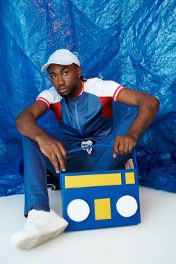 Genç, yakışıklı bir adam gururla oturur. Renkli bir müzik kutusuyla, parlak mavi bir arka plana karşı..