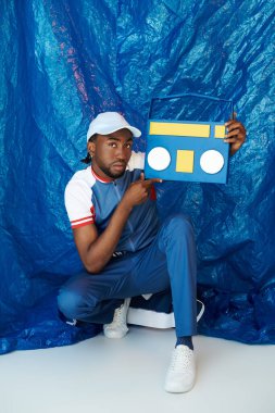 Yakışıklı genç adam, parlak mavi bir arka fona karşı gelişigüzel giyinirken klasik müzik kutusunu sergiliyor..