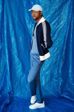 Genç bir adam kendine güvenerek şık kıyafetini cesur bir mavi arkaplanda sergiliyor..