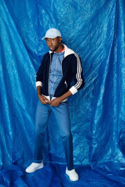 Yakışıklı bir genç adam şık bir şekilde duruyor mavi bir arkaplanın önünde neşeli bir ifadeyle.