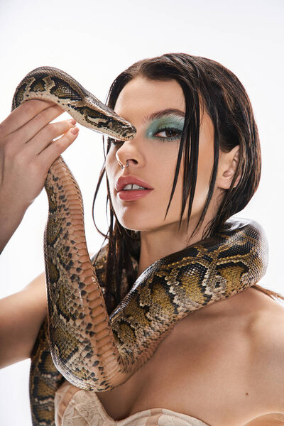 A young beautiful woman confidently poses with a snake elegantly coiled around her shoulders.