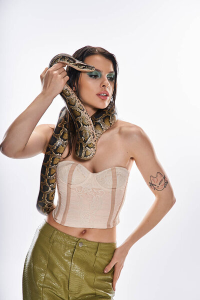 Молодая красивая женщина уверенно позирует, держа в руках змею, демонстрируя свою привлекательность и храбрость.