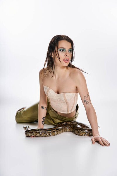 Молодая женщина позирует со змеей, смешивая красоту и опасность в минималистской студии.