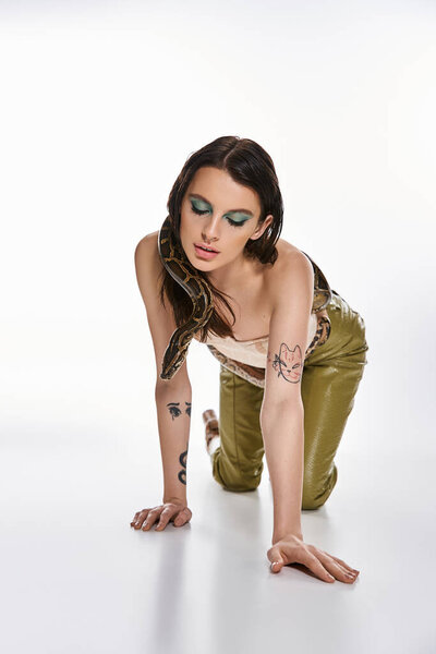 Потрясающая молодая женщина изящно преклоняет колени, в то время как змея обнимает ее, источая очарование и возбуждение..