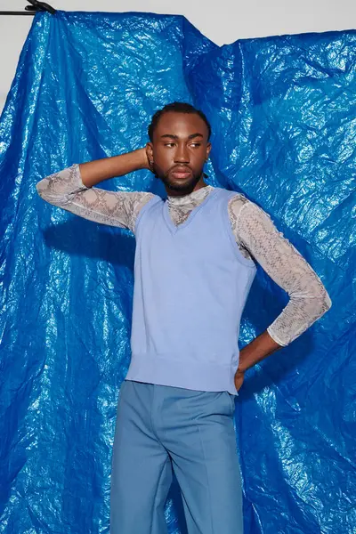Şık bir genç adam dikkat çekici bir mavi zemine karşı özgüvenle poz verir..