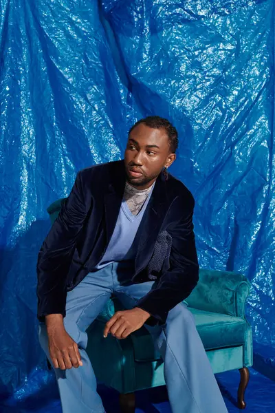 Kendine güvenen genç bir adam mavi dekorun ortasında zarif bir şekilde oturuyor..