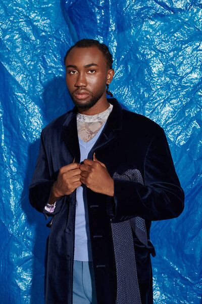 A stylish young man displays his fashion sense amid a striking blue background.