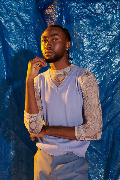 A stylish young man stands confidently against a striking blue background.