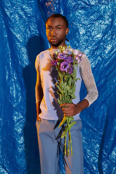 A handsome young man stands proudly with a bouquet of flowers, showcasing elegance and charm.