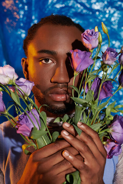 A confident young man presents a colorful bouquet against a blue background.