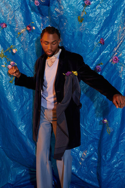 A handsome young man poses confidently against a striking floral blue backdrop.