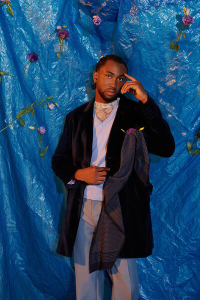A handsome young man stands poised in stylish attire, enhancing the blue backgrounds allure.