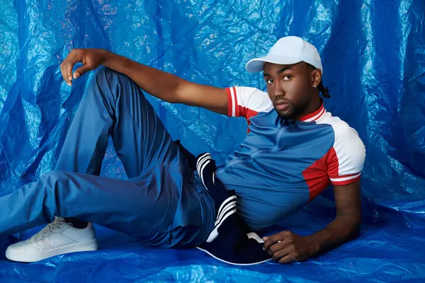 Yakışıklı genç bir adam zarif bir mavi yüzeyde uzanır, karizma ve stil yayar..