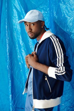 Kendine güvenen genç bir adam dikkat çekici mavi bir arka planla kendine has spor tarzını sergiliyor..