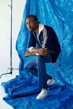 Şık bir genç adam, modern zarafeti gösteren parlak mavi bir arka plana karşı düşünceli bir şekilde poz verir..