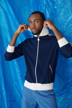 Genç bir adam tarzını ve güvenini düşünceli bir ifadeyle ve donanma kıyafetiyle sergiliyor..