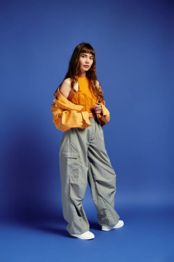 Şık, genç bir kadın, parlak mavi bir arka plana karşı şık bir elbise içinde poz veriyor..