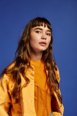 Genç bir kadın kendine güvenerek şık kıyafetini canlı bir mavi arkaplana karşı gösteriyor..