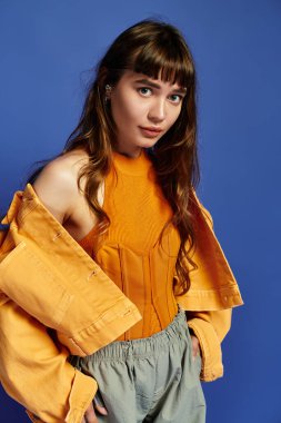 Kalın turuncu elbiseli genç bir kadın, parlak mavi bir arkaplanda poz veriyor..